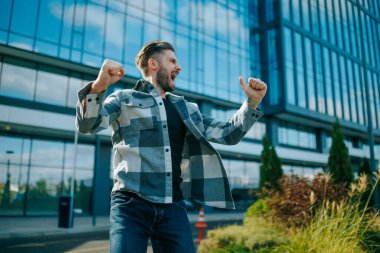 Gerçek başarıyı temsil eden sakallı genç bir adam açık havada zaferini kutluyor. Bu özgün portrede mutluluğu su götürmez..