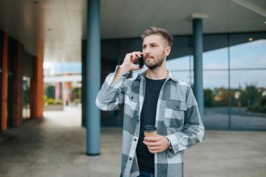 Kendine güveni tam bir Amerikan erkeği, elinde fincanla şehirdeki akıllı telefonu üzerinden canlı bir tartışmaya girişiyor. Bir Şehir Ayarında Telefonda Yakışıklı Erkek Tarzı ile Sohbet