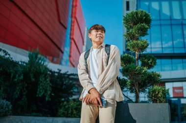 Yakışıklı bir Asyalı gencin canlı bir şehir portresi. Açık hava ortamında neşe ve memnuniyet saçıyor. Mutlu Asyalı Koreli Öğrencinin Şehir Portresi