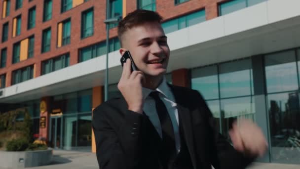 一位身穿西装打领带的拉美白人年轻商人 一边打电话一边享受着成功的喜悦 一边站在城外 背后是大楼 — 图库视频影像
