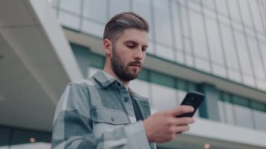 Güzel bir gülümsemesi olan yakışıklı bir adam, dışarıda cep telefonuyla internette sörf yapıyor. Hoş Şehir Anları Yakışıklı Adam ve Telefonu
