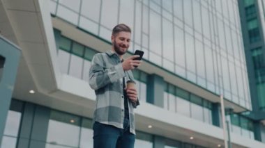 Şehir manzarasının ortasında, neşeli bir genç adam dijital dünyayla bağlantı kurmak için bir dakikasını ayırıyor. Akıllı telefonu açık hava deneyimine neşe katıyor..