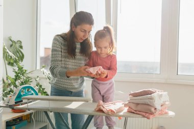 Otantik Anlar Genç Bir Anne ve Kız Evde Ütü Yaparken Uzun süreli Anılar Oluşturur. 4K Ev İşi ve Kaliteli Zamanda Aile