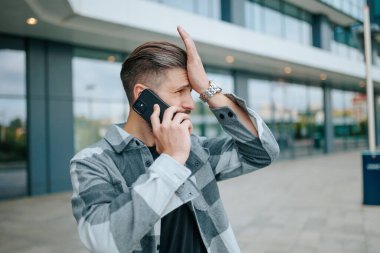 Endişeli ve endişeli bir genç sakallı adam şehir merkezinde telefonla konuşuyor. Sakallı bir erkek dışarıda endişeli bir telefon görüşmesi yapıyor.