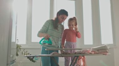 Aile Sevgisi Bir Anne ve Kızı Birlikte Değerli Zaman geçirip Ev İşlerinin Gerçek Yaşamını Gösteriyorlar. Otantik Aile Anları Evde Giysiler Ütülüyor