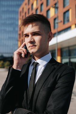 Şehrin ortasında dikey çekim yapan, takım elbiseli genç, profesyonel bir adam akıllı telefonuyla bir konuşma yapıyor, fotokopi alanı sağlıyor, iş başındaki beyaz yakalı işçiyi canlandırıyor..
