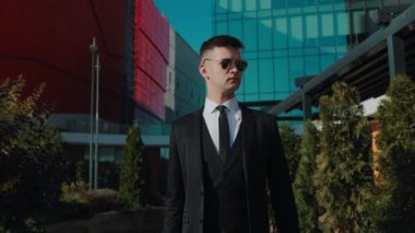 Modern ofis binalarının arka planında, takım elbiseli beyaz Amerikalı genç bir adam profesyonel ve azimli bir girişimci imajı çiziyor..