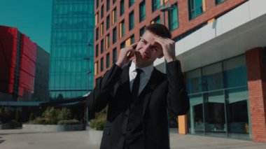 Açık bir şehir diyaloğunda, düşünceli ve düşünceli bir iş adamı, keskin bir iş elbisesi içinde, canlı şehir manzarasının ortasında akıllı telefonuyla konuşur..