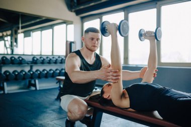 Kendini adamış bir erkek antrenör, spor salonunda bir kadına dambılı kaldırmasında yardımcı olur. Spor Salonu Erkek Antrenörü Aptal Kaldıran Kadın Asistanı