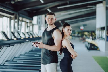 Dinamik ikili. Bir adam ve kadın spor salonunda poz veriyor, kamerada gözleri var. Genç Bir Erkek ve Bir Kadının Kararlı Spor Salonu Portresi. Spor Giysilerinde İki Kişinin Beden Bağlantısı Portresi