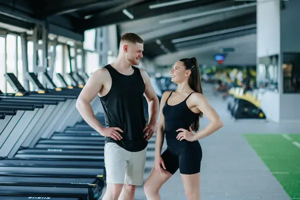 Spor salonunun güçlü çifti kararlı ifadeleri olan genç adam ve kadın, kamera görüntüsü. İki Kararlı Kişinin Kamera-Hazır Spor Salonu Portresi