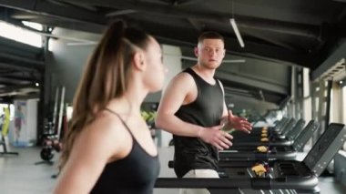 Beyaz bir erkek antrenör, spor salonundaki yüksek yoğunluklu egzersiz sırasında genç bir İspanyol kadına rehberlik ediyor. Spor salonunda Erkek Özel Eğitmeniyle Koşan Aktif Genç Kadın
