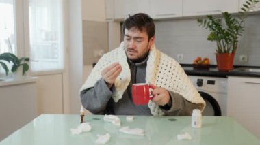 Gerçek bir anı yakalayan bu fotoğraf, evde grip ilacı alan stresli bir adamı gösteriyor. Mutfak sandalyesinde otururken acı çekmenin nüanslı gerçeklerine objektif bir bakış sunuyor.