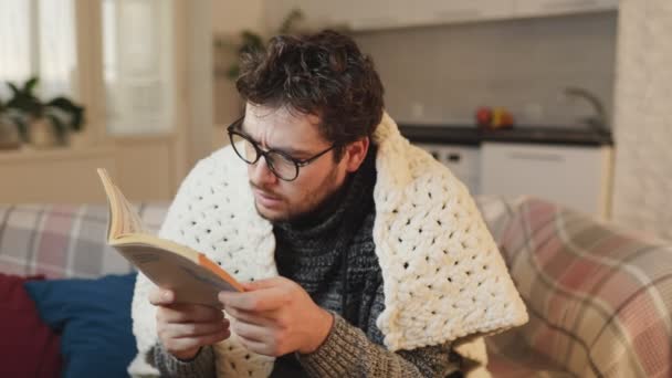 絶望的な読者 眼鏡をかけた男 書物に没頭し 驚きを覚え 彼の無熱のアパートで羽毛布団の下で暖められる ととも — ストック動画