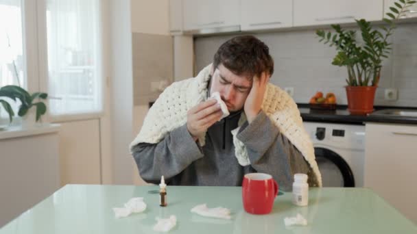 年轻人在与流感作斗争的过程中 在家里裹着羽绒被 经历着压力和痛苦 坐在厨房的椅子上 他打喷嚏或咳嗽 用客观的视觉观察季节性的色调和疾病 — 图库视频影像