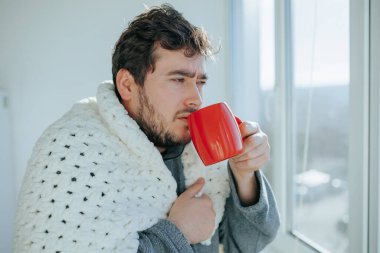 Tarafsız gerçekçilik, evde battaniyeye sarılı sakallı bir adam mutfak sandalyesinde grip ile uğraşıyor, bardaktan su içme eylemiyle meşgul. Mevsimsel Hastalıklarla Başa Çıkan Gerçek Görüntü Sakallı Adam