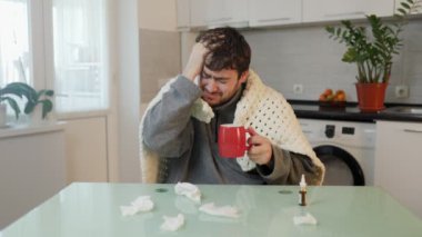 Sakallı bir adam evde yorgana sarılı baş ağrısı ve griple başa çıkar. Bu samimi bakış açısı mevsimsel hastalıkların getirdiği zorluklara dürüst bir perspektif sunar.