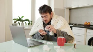 Mevsimlik bir rahatlık. Sakallı bir adam, rahat bir battaniyenin altında, evindeki mutfaktaki bilgisayarının yanında grip hapları alıyor. Mevsimsel hastalıklarla azim ve dirençle savaşıyor..
