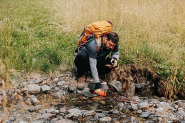 Hidrasyon Uyumu Latin Gezgin Susuzluğunu Söndürüyor, Bir Şişeyi Temiz Nehir Suyuyla Dolduruyor.