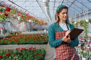 Çiçekçi kız, elinde defterle serada çalışıyor. Kadın çiçekleri analiz ediyor, çiçekçi bahçe uzmanı, kopyalama alanı.