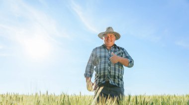 Yazın kırsal kesimde tarım çiftliğinde dikilirken kameraya başparmağıyla bakan olgun bir erkek işçi. Gülümseyen çiftçi, fotokopi alanında baş parmağını gösteriyor.