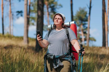 Bir Amerikan yürüyüşçüsünün dünyasına adım atın, doğa ve teknoloji arasındaki dengeyi gösterin, şişman bir kadın yürüyüşü sırasında dinleniyor, akıllı telefon rahatlığının tadını çıkarıyor..