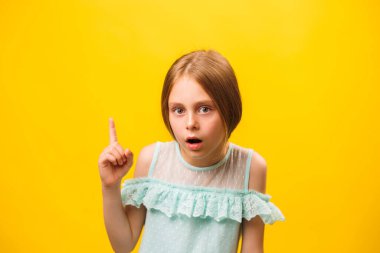 Fikir, şaşırmış küçük Amerikalı kız çocuğu sarı arka planı işaret ediyor. çocuk uyarısı ve çocukluk konsepti, kopyalama alanı