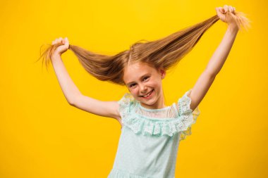 Komik kız kameranın önünde surat asıyor. Çocuk elleriyle saçını tutuyordu. Sarı arka planda duruyor. çocuklar ve kopyalama alanı