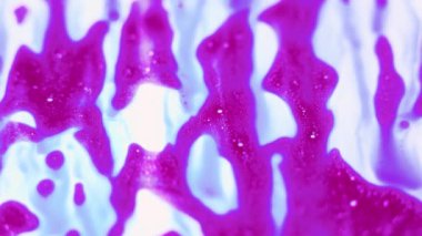 Parlak yağlı boya beyaz boya üzerinde zarif bir şekilde suyla akar ve güzel bir mavi ve pembe renk karışımı yaratır. Seçici odaklı soyut arkaplan bu canlı ve dinamik videoya derinlik ekler.