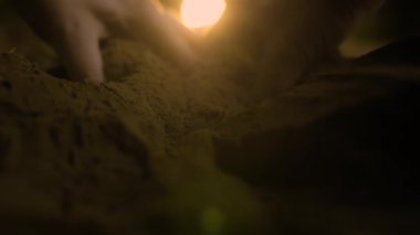 Toprağı eşeleyen bir insan elinin yakından çekimi, parmaklar ve arka plandaki yemyeşil bahçe üzerine seçici bir odaklanmayla.