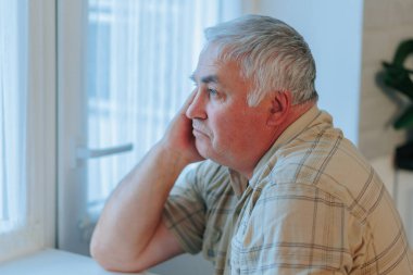 Yalnızlığın ifadesi düşünceli bakışları ve yaşlı bir erkeğin çatık kaşlarını gösteren bir yan bakış açısı, evdeki iç gözlem, üzüntü ve depresyon hissini iletiyor..