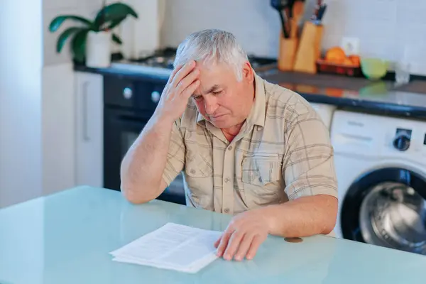 Frustrated elderly man receives a dismissal letter, depicting realistic emotions of sadness and financial distress in a home setting.