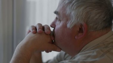 Düşünceli bir bakışla yaşlı bir adamın ciddi ve yansıtıcı yüzünü yakalıyor, evde tek başına oturuyor, yaşlanan yolculuğunun zorluklarını ve yalnızlığını düşünüyor..