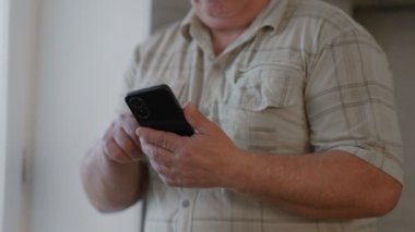 Çevrimiçi Dünya 'da gezinen yaşlı bir adam akıllı telefonunu evdeki interneti taramak için kullanıyor ve teknolojinin günlük hayatına entegrasyonunu vurguluyor..