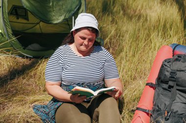 Bir Amerikan yürüyüşçüsünün iyi bir kitaptan huzur bulması için yaptığı yürüyüş sırasında doğa ve okumanın uyumuna tanık olun. Sırt çantası ve çadırının yanında otururken sakinliğini hisset.,