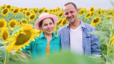 Front view of happy farmers family in a field with sunflowers, looking at the camera and at each other. Young man and woman are happy they have a rich harvest. Background sunflowers and copy space