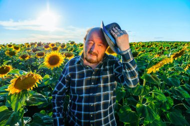 Tired exhausted farmer touching forehead standing in cultivated sunflower field. Farmer work hard against poverty. Feeling and emotion expression. Agriculture