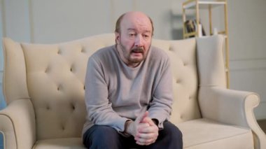 Üzgün bakışlı yaşlı bir adam kanepeye oturur ve uzak bir yere bakar. Alzheimer bir adamı saygıdeğer bir yaşta vurdu. Uzaktan bir bakış, düşüncesi yok, boynunda atkı, ölüme mahkum bir bakış. Ön görünüm.