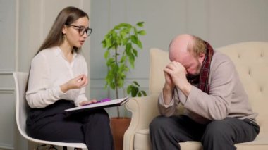 Genç ve güzel bir kadın psikoloğun resepsiyonundaki yaşlı adam ölüme mahkum bir vaziyette oturuyor. Yaşlanma kavramı, genç yaşlılar, psikolojik yardım, psikolog ofisi. Bulanık, seçici.