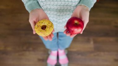 Donut ve elmayı, tartının üzerinde duran tanınmayan bir kadının ya da kızın elinde kapat. Tercih edilen un. Diyet olsun. Elde tatlı çörek, elde elma, kırmızı elma, sonsuz diyet. Güzellik ve sağlık kavramı.