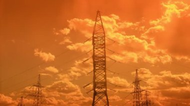 Büyüleyici bir zaman atlaması, çarpıcı bir günbatımının arkaplanına karşı yüksek voltajlı elektrik hatlarının karmaşık ağını sergiliyor, teknoloji ve doğanın sinerjisini gösteriyor..
