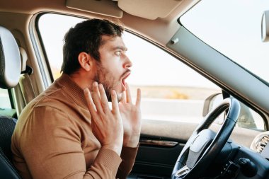 The screaming young man behind the wheel of the car let go of the steering wheel, stopping the car. Something terrible happened on the road, the guy saw it and got scared. Emotions and people. clipart