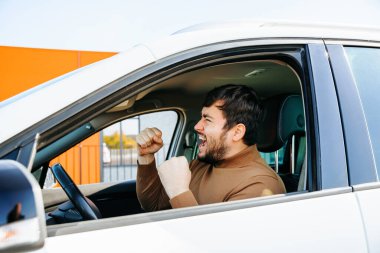 Kafkas sakallı genç sürücü çıldırmış ve kızgın bağırıyor. Yakışıklı insanlar ve direksiyondaki stres kavramı, jestler, yan profil.