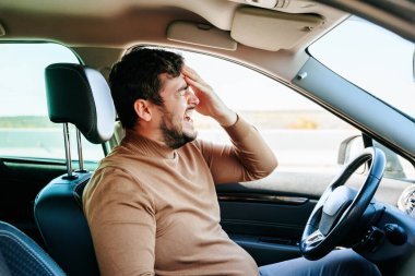 Gözleri kapalı, ağzı ve sakalı açık genç bir erkek. Şoför arabada oturuyor ve baş ağrısı ve nevraljiden muzdarip. Etkileyici yüz ifadesi..