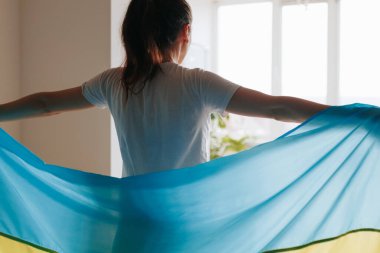 Evinin penceresinde Ukrayna bayrağını tutan ve ülkesine bağlılığını ifade eden bir kadının sırtı kameraya dönük..