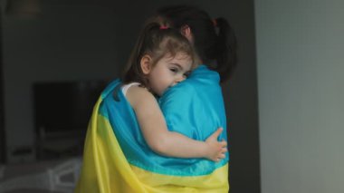 Evlerinin sınırları içinde, her ikisi de Ukrayna bayrağıyla süslenmiş, ülkesine ve ailesine olan bağlılıklarını simgeleyen çocuğunu gururla kucaklayan bir kadın..