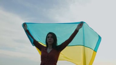 Ukrayna bayrağını bir tepenin üstünde enerjik bir şekilde dalgalandıran genç bir kadın olarak vatanseverliğin dinamik tasvirine bakın. Hareketleri Avrupa yıldızları altında birleşmiş bir ulusun özlemlerini yansıtıyor..