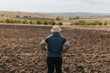 Agricultural Wisdom Senior Farmer Analyzing Soil in Autumn Harvest. Harvest Portrait Aged Farmer with Mustache Examining Farmland, back view clipart