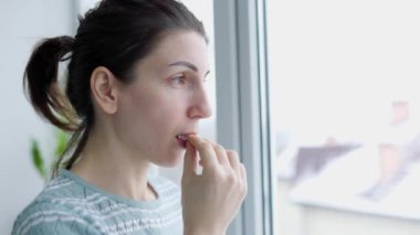 Antiviral hapları yutan bir kadının elindeki bir bardak suyu kapat. Başı ağrıyormuş. Kendi sağlığınla ilgilenmek. Evde, içeride. Pencerede.