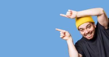 Fotokopi uzayı olan bir stüdyo resmi. Boş alanı işaret eden, neşeli bir jest ve mutlu bir ifadeyle kameraya bakan, etkileyici sakallı bir adam. mavi arkaplan, sarı başlıklı